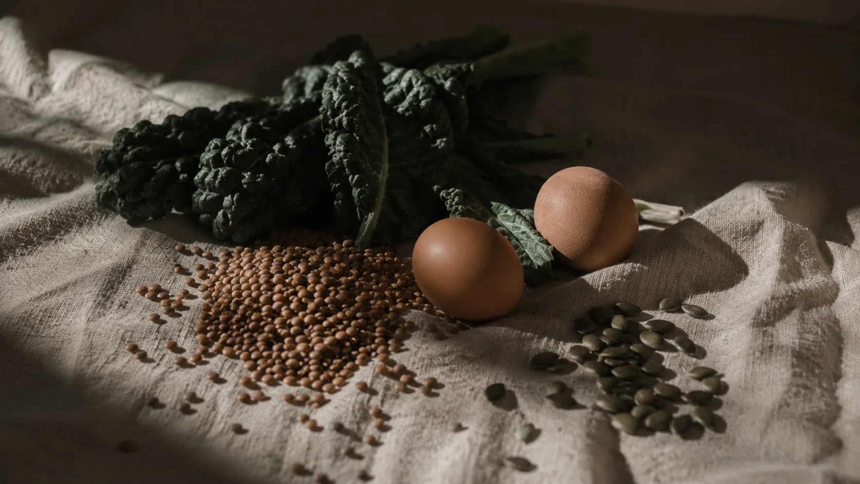 Lentils, kale, eggs and pumpkin seeds on linen in low daylight.